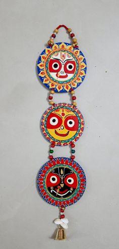 three colorful masks hanging on a wall next to a bell ornament with bells