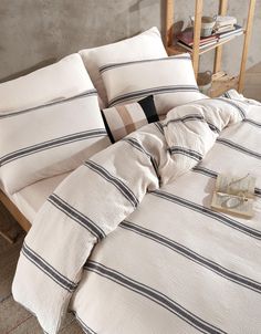 an unmade bed with black and white striped comforter on the bottom, next to a book shelf