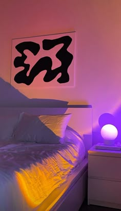 a white bed sitting under a purple light in a bedroom next to a night stand