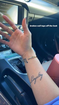 a woman with her hand on the steering wheel of a car, showing off her tattoo