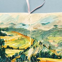 an open book with watercolors on it and a ribbon hanging from the cover