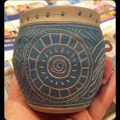 a hand holding a blue vase with designs on it