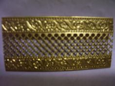 a gold metal object on a white surface with some sort of design in the middle