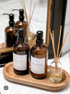 three bottles of soap and reeds on a wooden tray in front of a mirror