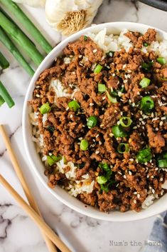 a white bowl filled with ground beef and green onions next to chopsticks on a marble surface