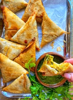 a person dipping some food into a bowl with salsa in it and tortilla chips on the side