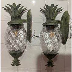 two glass pineapple shaped wall sconces with green leaves on the top and bottom