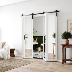 a living room with white walls and wooden floors, two sliding doors open to reveal a dining area