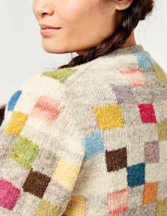 a woman with braids in her hair wearing a multicolored sweater and hat