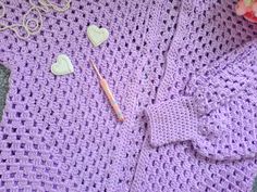 a crocheted purple sweater with hearts on it next to flowers and a pencil