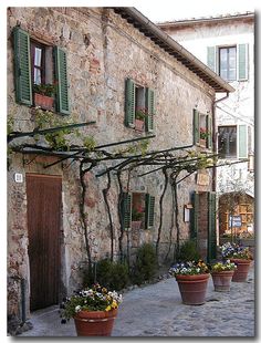 an old stone building with green shutters and potted plants