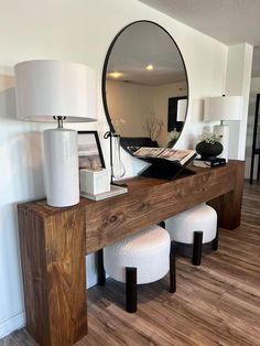 a wooden table topped with a mirror and two stools next to a white lamp