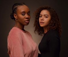 two women standing next to each other in front of a dark background