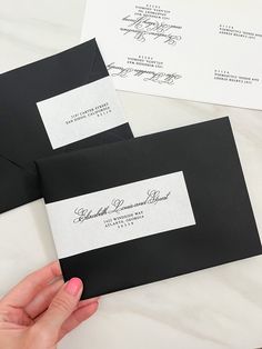 two black envelopes with white address cards on them are being held by a woman's hand