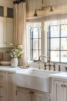 a white kitchen sink sitting under a window next to a counter top with flowers on it