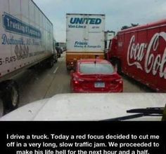 a red car driving down a street next to trucks and other traffic on the road