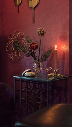 a table with flowers and candles on it in front of a purple wallpapered room