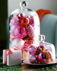 a glass clochet filled with christmas ornaments next to a gift box on a table