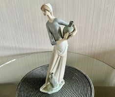 a ceramic figurine holding a vase on top of a glass table