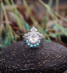 an engagement ring on top of a rock in front of some grass and rocks with blue stones