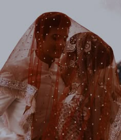 a man and woman dressed up in wedding attire standing next to each other with veils over their heads