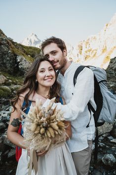 a man and woman standing next to each other in front of mountains with snow on them