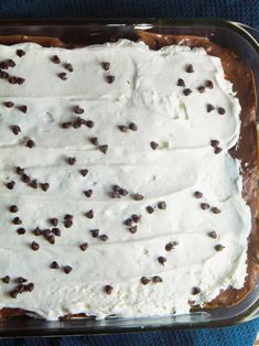 a cake with white frosting and chocolate chips on top in a glass dish sitting on a blue towel