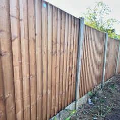 a wooden fence next to a field with grass and dirt on the ground in front of it