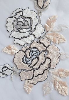 embroidered roses on white fabric with gold leaves and beads are featured in this close up photo