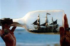 a ship in a bottle is being held up by someone's hand with the ocean in the background