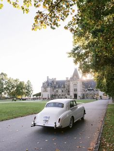 an old white car is parked in front of a large house on the side of a road