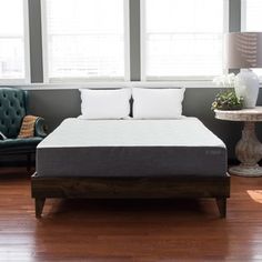 a bed sitting on top of a wooden floor next to two windows