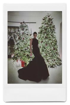 a woman in a black dress standing next to a christmas tree with presents on it