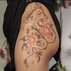 a woman with a dragon tattoo on her lower back and side thigh, holding flowers