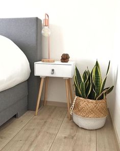 a bedroom with a bed, nightstand and plant on the floor in front of it