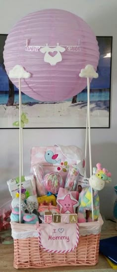 a pink basket filled with baby items on top of a wooden table next to a painting