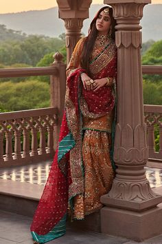 a woman in a red and gold sari leaning against a light pole on a balcony