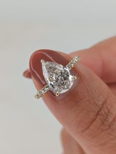 a woman's hand holding an engagement ring with a pear shaped diamond