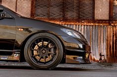 a black car with gold rims parked in front of a fenced off area