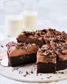 a chocolate cake on a plate with two glasses of milk