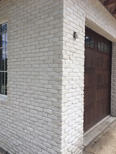 a white brick building with a brown door and window on the side of the building