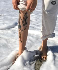 a person standing in the snow with tattoos on their legs and feet, holding something