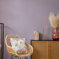 a wicker chair next to a wooden cabinet with a vase on top of it