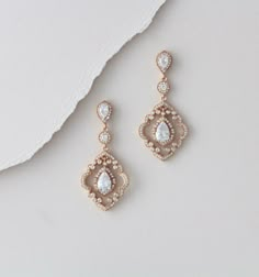 two pairs of gold earrings with white stones on the bottom and one has a tear shaped drop