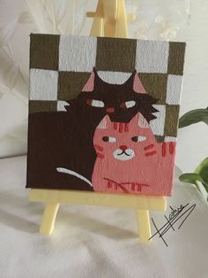 an easel with a cat painting on it next to a potted plant in the background