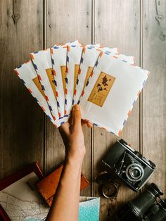 a person holding several envelopes in front of an old camera on a wooden table