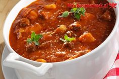 a close up of a bowl of stew on a table with a red and white checkered napkin