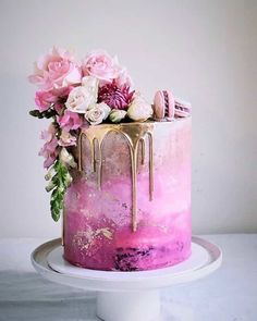 a pink cake with gold drips and flowers on the top is sitting on a white plate