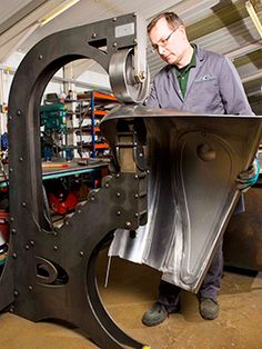 a man standing next to a machine in a room with lots of tools on it