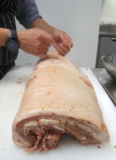 a person cutting up a large piece of meat on top of a white cutting board